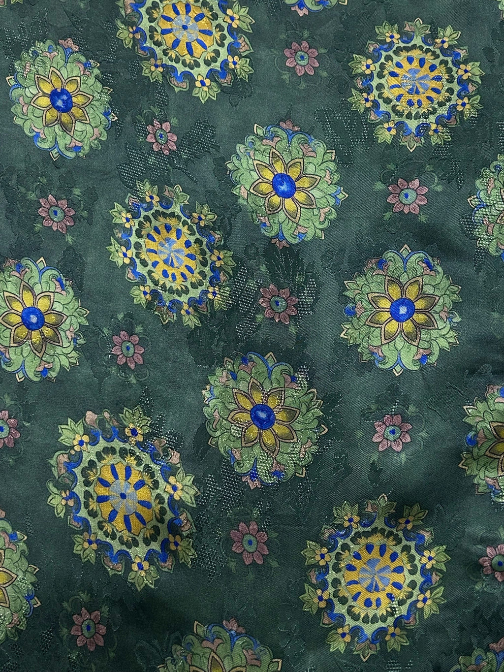 Close-up of dark green fabric covered in repeating ornate floral medallions in blue, yellow, pale green, and muted pink.