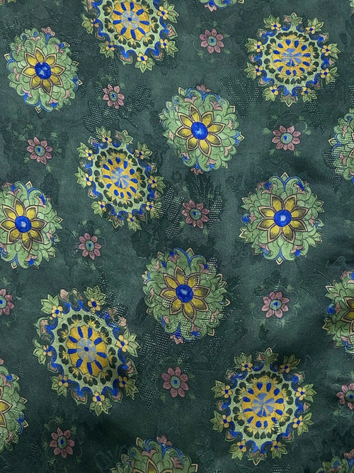 Close-up of dark green fabric covered in repeating ornate floral medallions in blue, yellow, pale green, and muted pink.