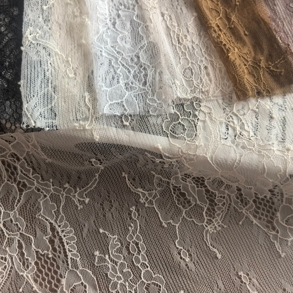 Layered lace fabric in black, ivory, white, and brown, with floral motifs and open mesh; several pieces are folded and draped together.