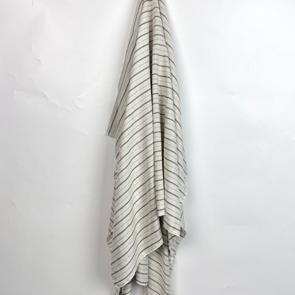 Off-white fabric with thin dark stripes hangs in long, overlapping folds against a plain white background.