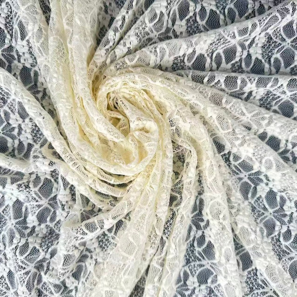 Close-up of ivory lace gathered into a spiral, with floral motifs and open mesh draped in curved folds.