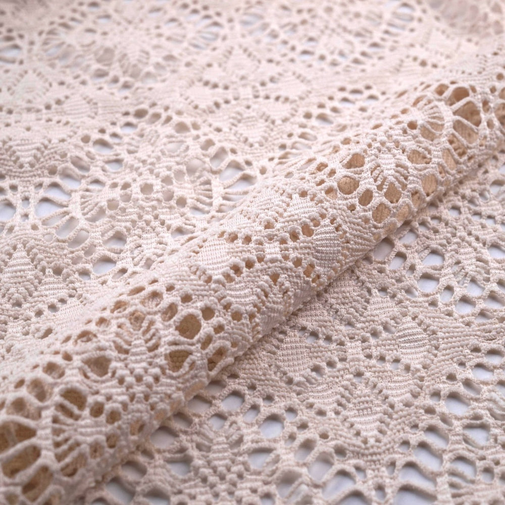 Close-up of ivory lace fabric arranged in overlapping folds, with an openwork floral and geometric pattern.