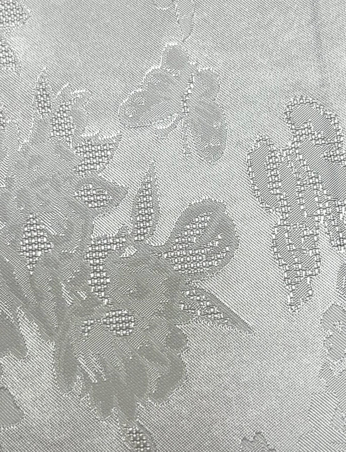 Close-up of silver-gray fabric with a subtle woven floral motif and scattered raised-looking details across the surface.