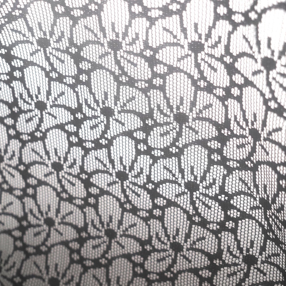 Close-up of black lace-like fabric with a dense floral and leaf motif; the pattern appears as dark outlines against a light background.