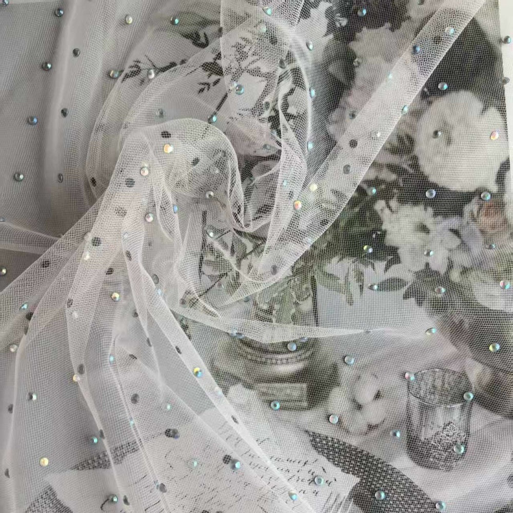 White translucent mesh is gathered into flowing folds, dotted with small iridescent embellishments, over a pale floral and leafy print.