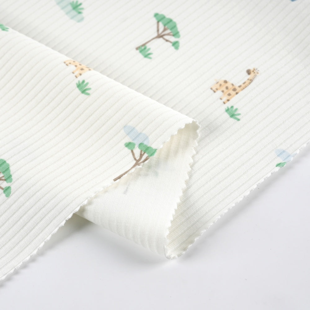 Close-up of a folded ivory cloth with fine diagonal ribbed lines and scattered green trees and tan, spotted giraffes.