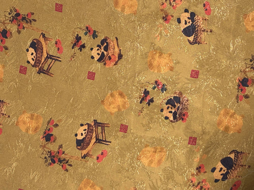 Close-up of gold cloth patterned with scattered stylized pandas, orange blossoms, dark branches, and small red square seals.