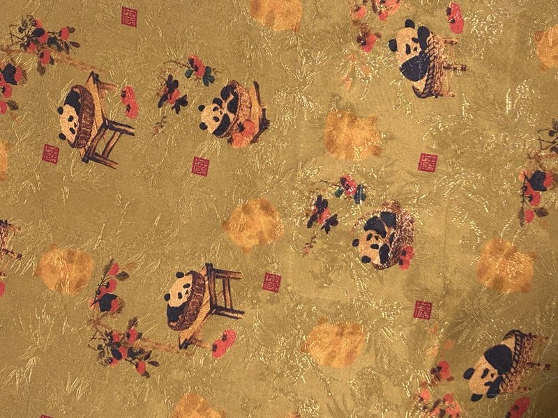 Close-up of gold cloth patterned with scattered stylized pandas, orange blossoms, dark branches, and small red square seals.