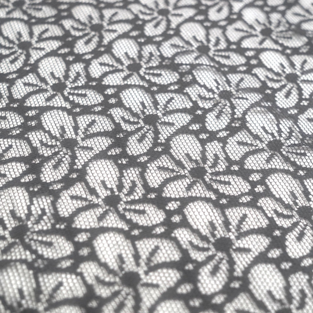 Close-up of black lace with repeating floral motifs and fine mesh between them, arranged across the frame.