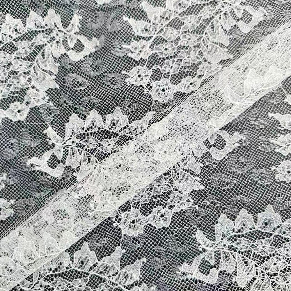 Close-up of white lace with dense floral motifs and fine netting, layered diagonally over a darker background.