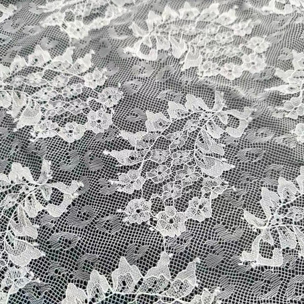 Close-up of white floral lace with an open net pattern and embroidered flower and leaf motifs arranged across the fabric.