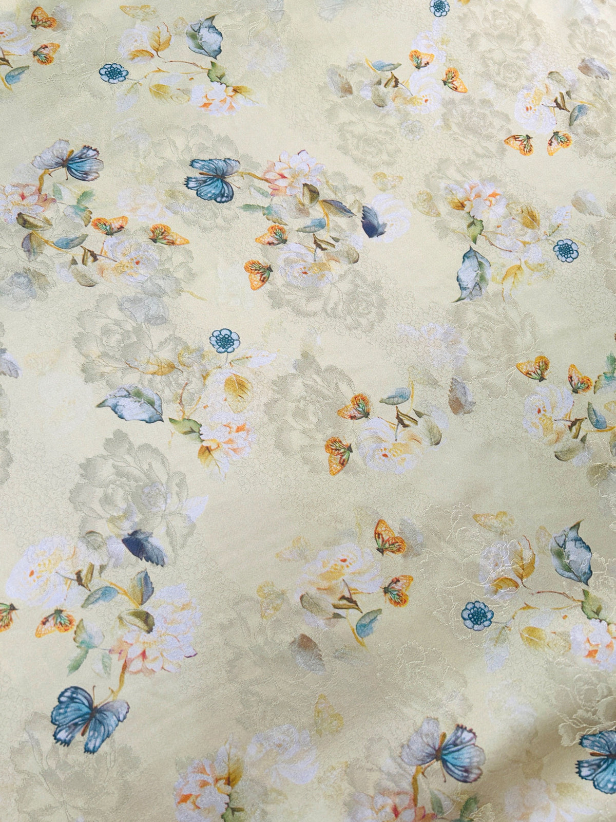 Close-up of pale cream fabric with a scattered floral pattern, blue butterflies, small teal flowers, and muted yellow, peach, and gray accents.