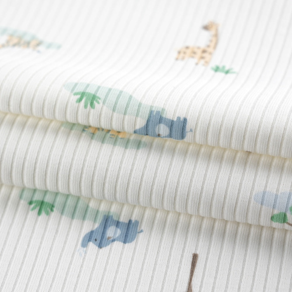 Close-up of white ribbed cloth printed with small muted blue and green animal and plant motifs, folded in layered curved drapes.