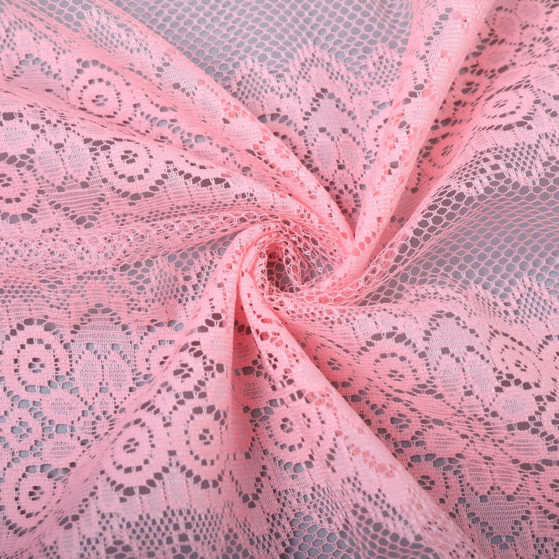 Close-up of pale pink lace fabric with repeating floral and geometric openwork motifs, draped in curved folds.