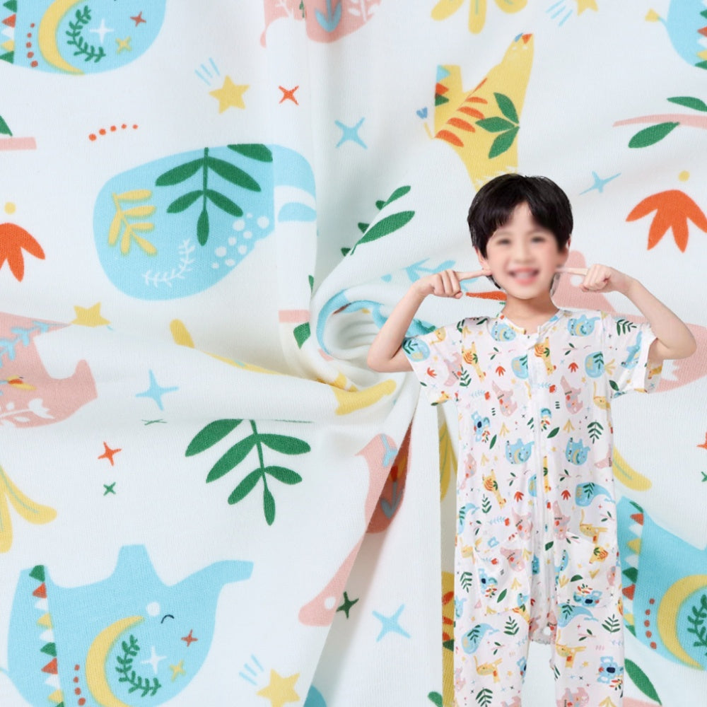 A close-up of white fabric printed with colorful animals, leaves, stars, and abstract shapes, with a draped section beside a child wearing a matching short-sleeved pajama garment.