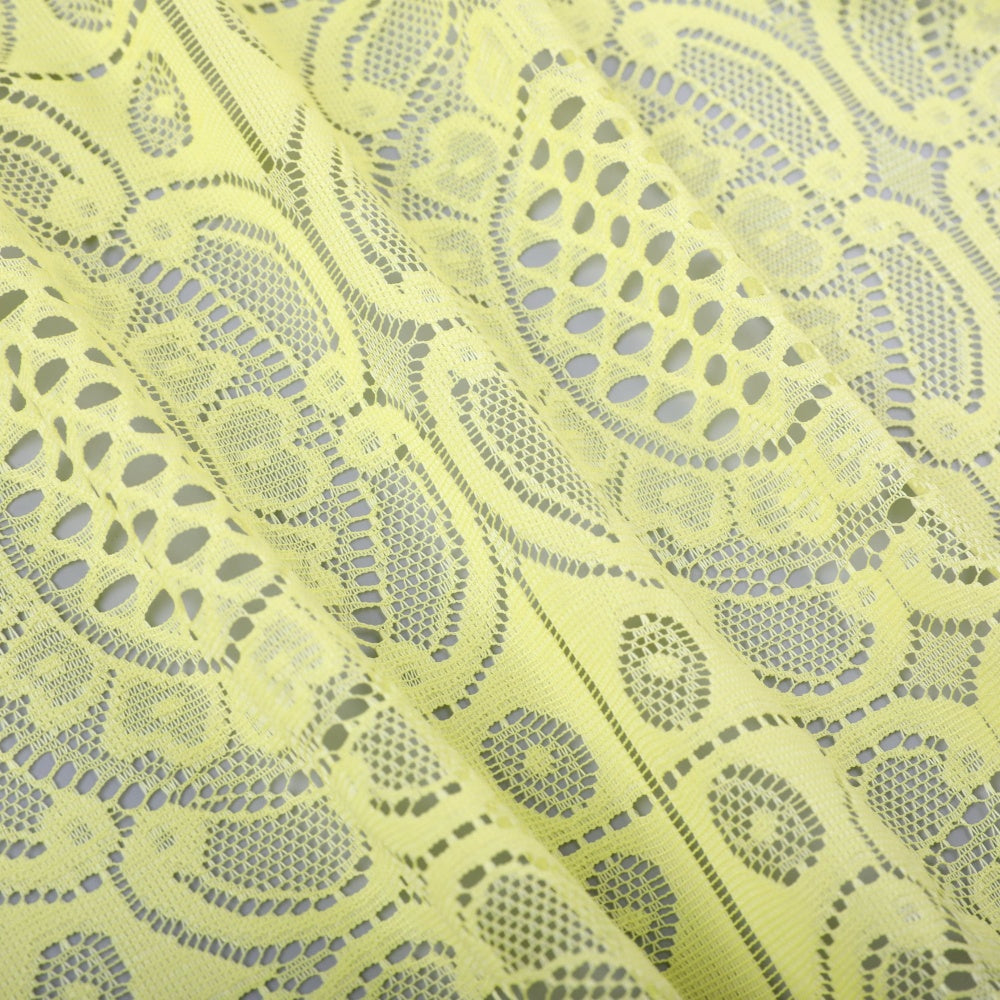 Pale yellow lace fabric with repeating openwork floral and geometric motifs, arranged in overlapping folds and photographed close enough to show the mesh detail.
