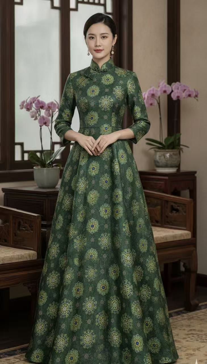 A full-length view of a woman wearing a floor-length dark green garment with an allover pattern of gold and pale green floral medallions with small blue centers.