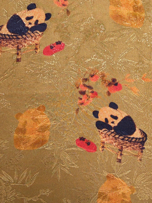 Close-up of gold-brown fabric with a textured woven pattern, scattered red and orange flowers, and two cartoon pandas seated in baskets; the cloth is shown flat.