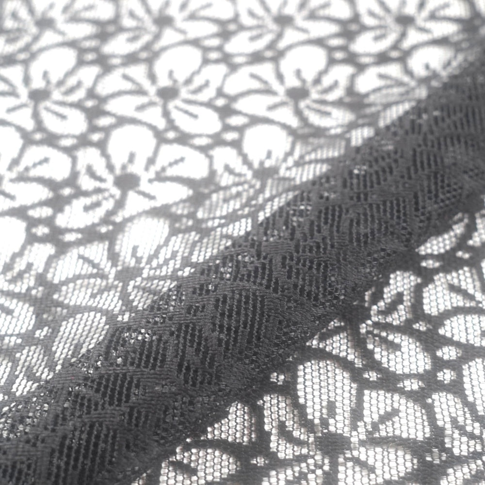 Close-up of black lace fabric with a repeating floral motif and open mesh, shown folded diagonally over itself.