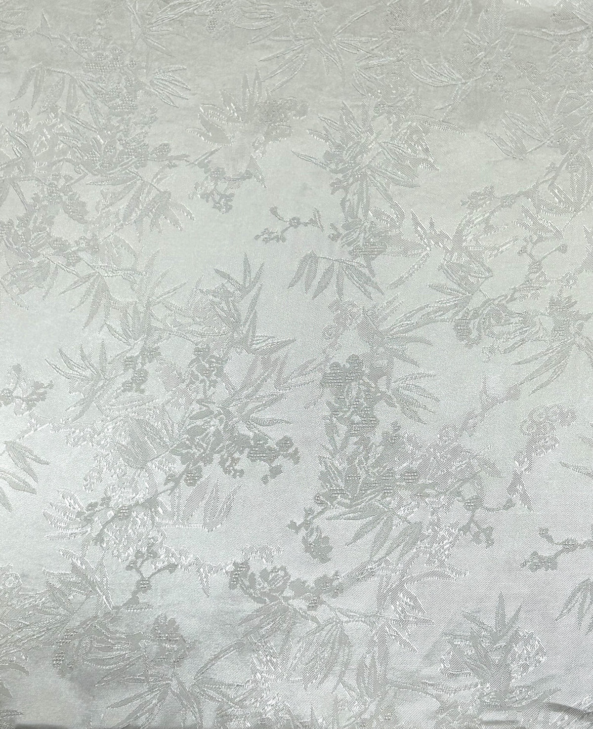 Close-up of a pale gray fabric swatch with a repeating, scattered botanical motif of leafy branches and small blossoms woven in slightly darker gray and silvery tones.
