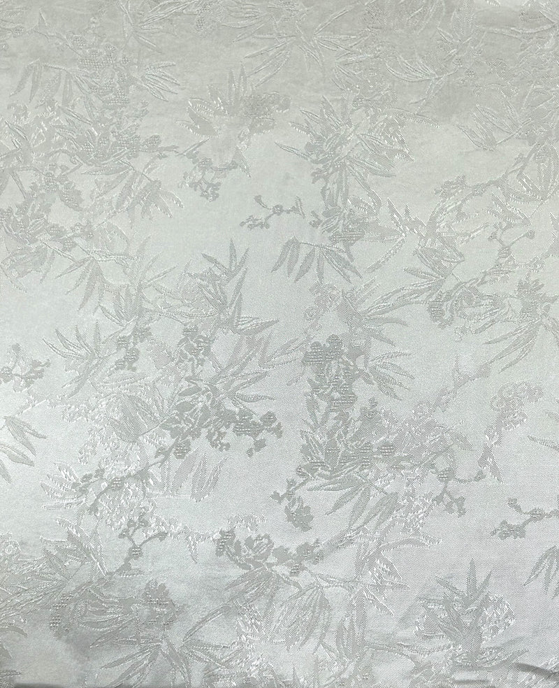 Close-up of a pale gray fabric swatch with a repeating, scattered botanical motif of leafy branches and small blossoms woven in slightly darker gray and silvery tones.