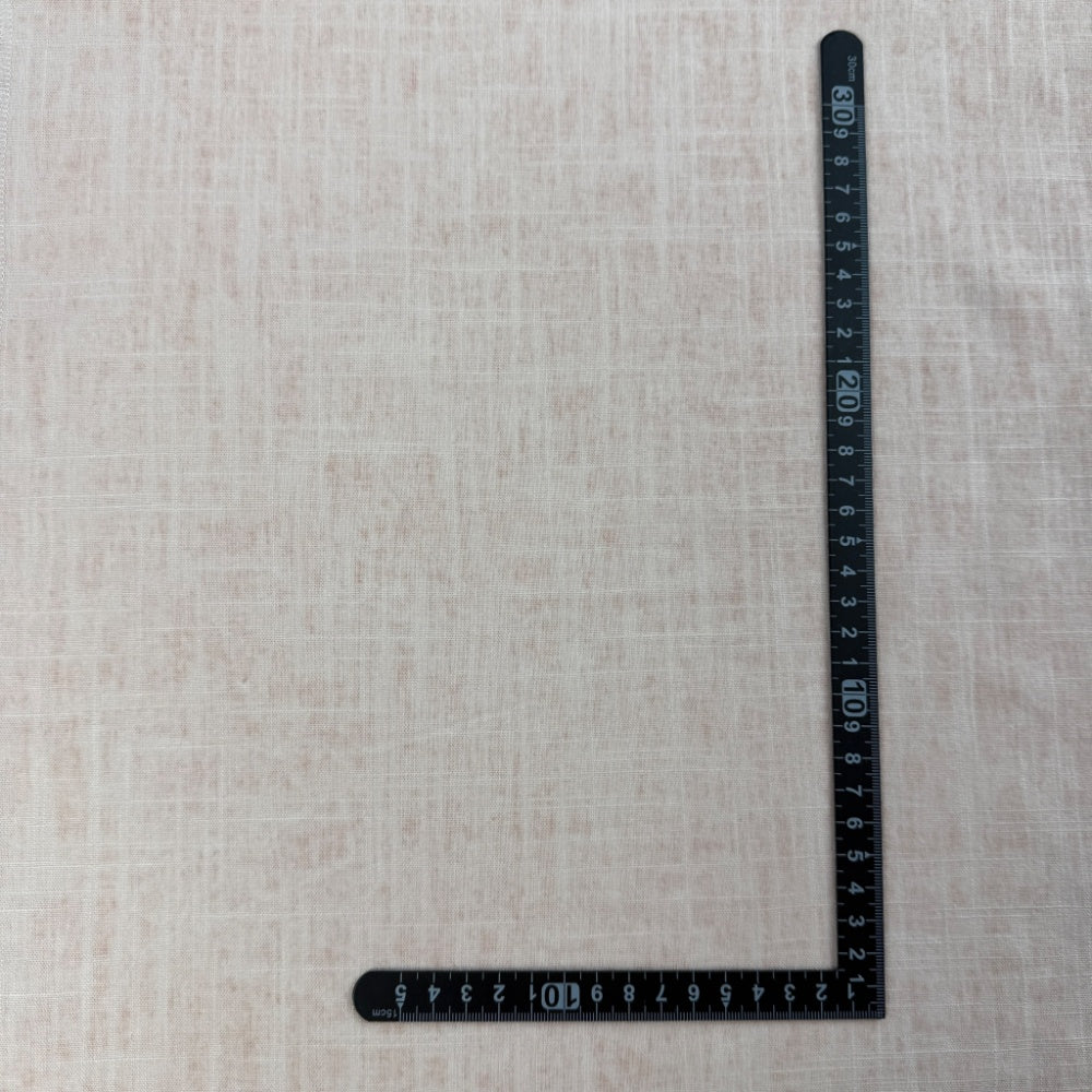 Pale blush and ivory fabric with a subtle irregular crosshatch weave is laid flat, with a black L-shaped measuring ruler along the right and bottom edges.