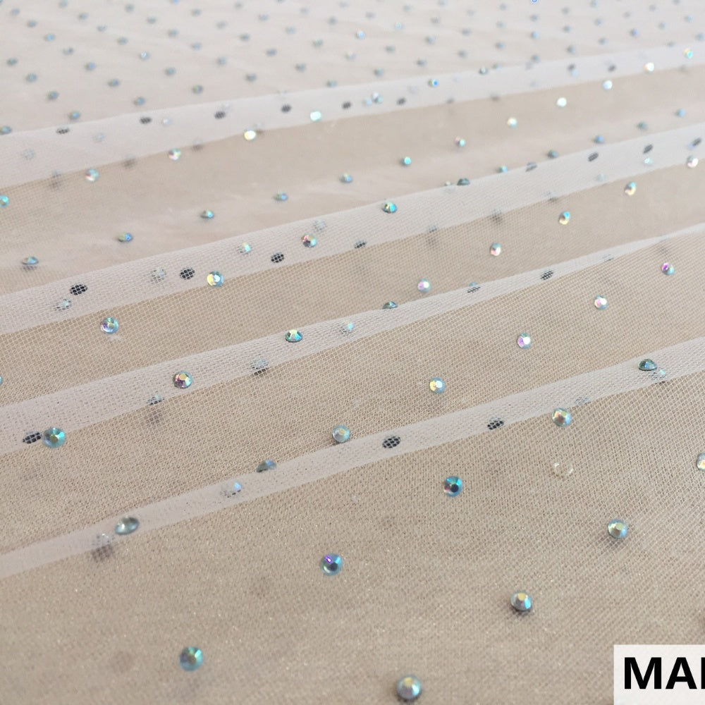 A close view of beige mesh fabric with scattered small iridescent sequins and dark spots, arranged in diagonal bands.