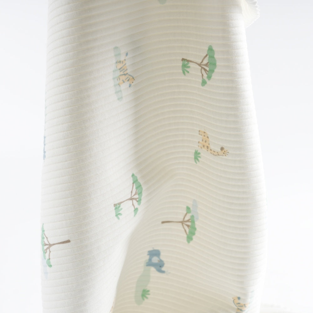 Close-up of pale ivory cloth with curved horizontal ridges and scattered muted green plant motifs and tan spotted animal shapes.