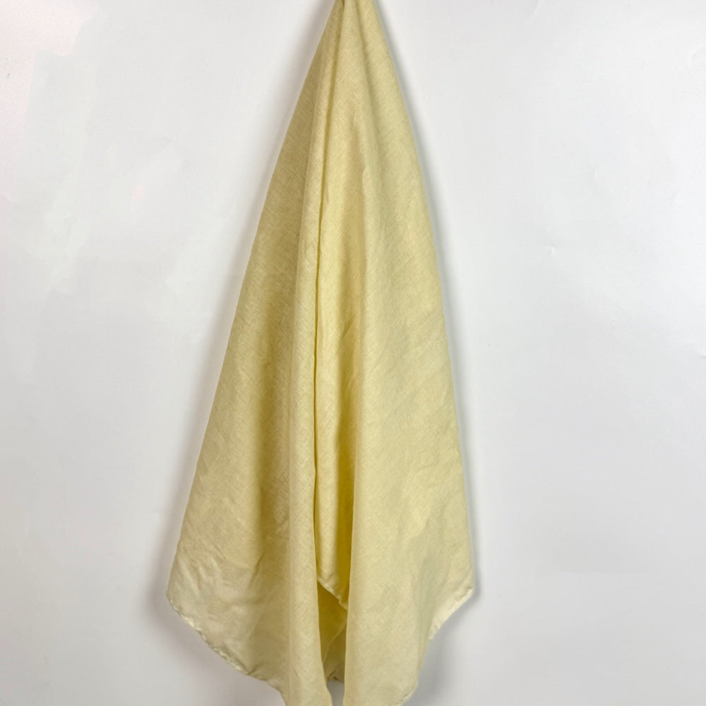A pale yellow cloth hangs in long draped folds against a plain white background; close-up view.