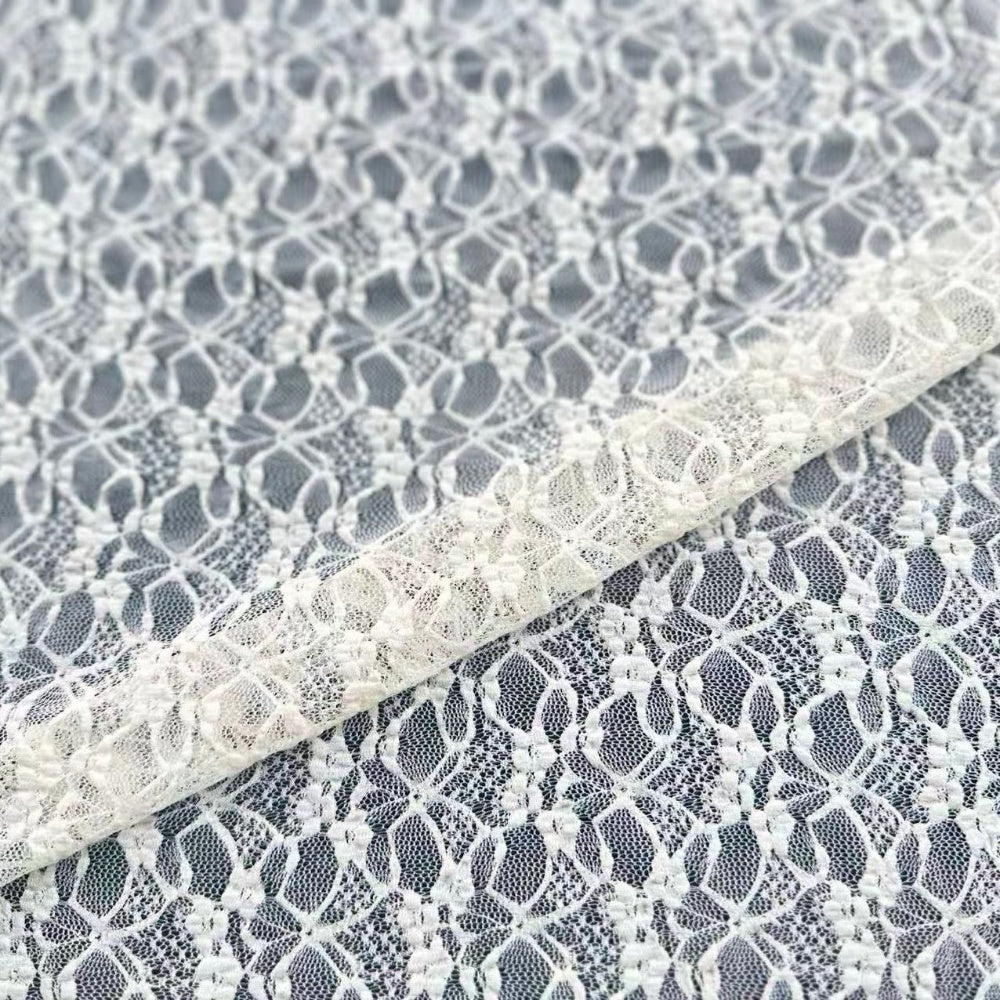 Close-up of white floral lace with a repeating openwork pattern, draped diagonally over matching lace on a gray background.
