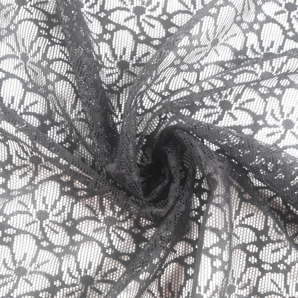 Close-up of black lace fabric gathered into a spiral, showing a dense repeating floral and geometric mesh pattern against a light background.