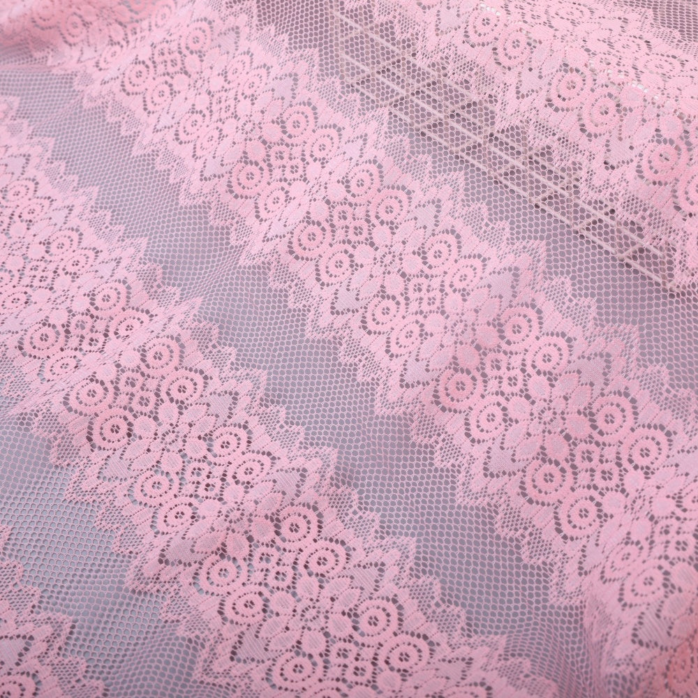 Close-up of pale pink lace fabric with repeating floral motifs and scalloped bands arranged diagonally across the frame.