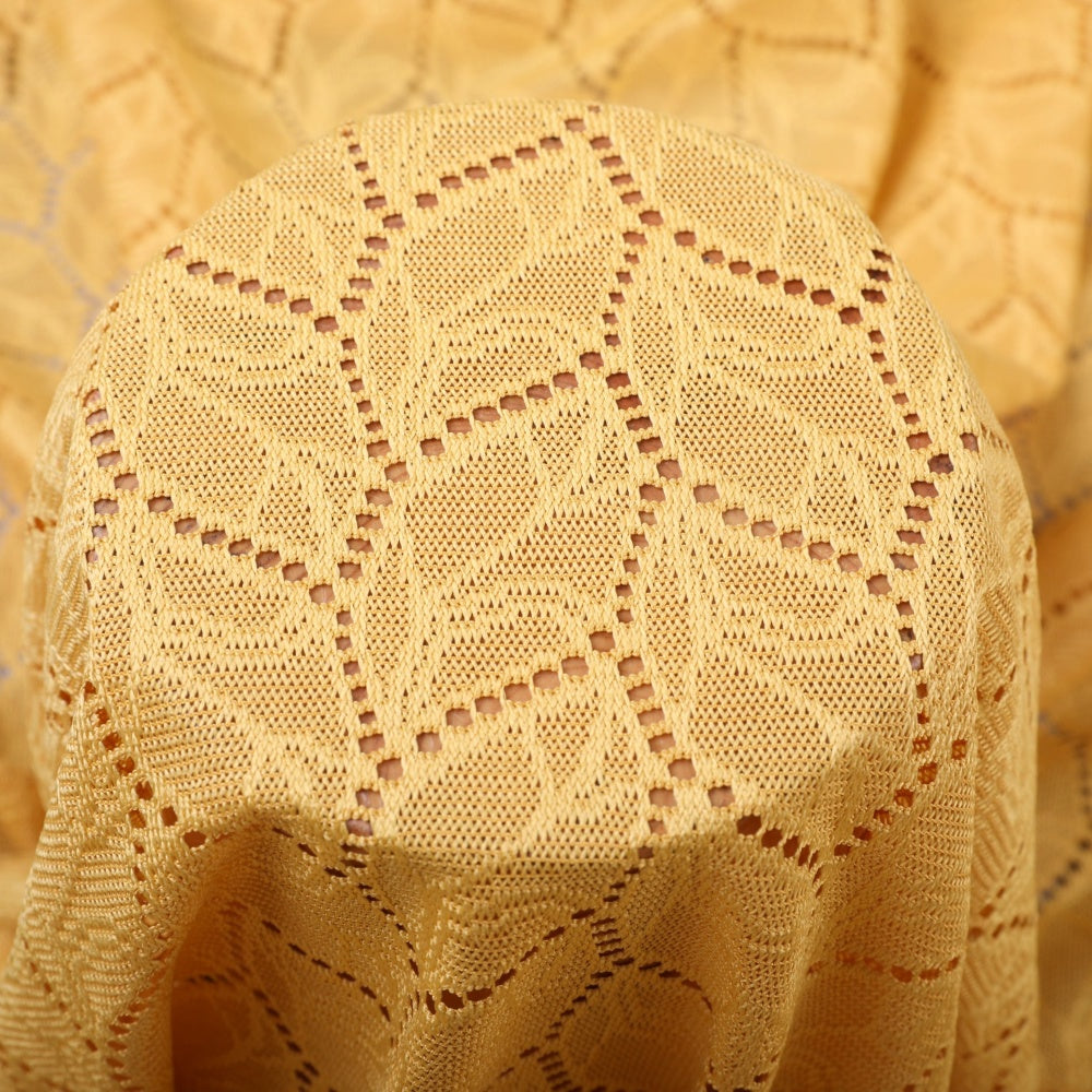 Close-up of pale golden cloth with repeating geometric openwork motifs, draped in curved folds.