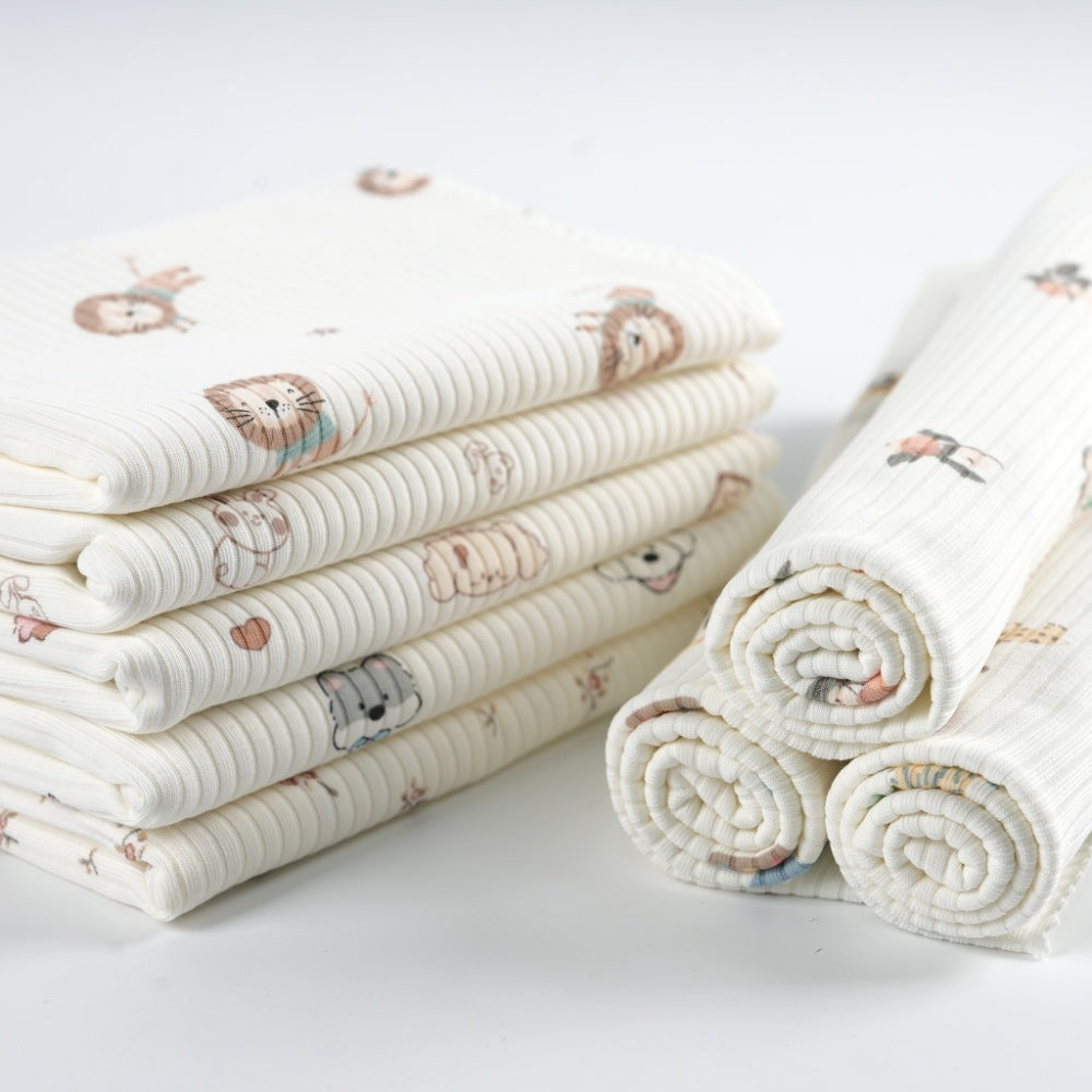Close-up of cream ribbed cloth with small muted animal motifs, arranged in a stack of folded pieces beside three rolled pieces.