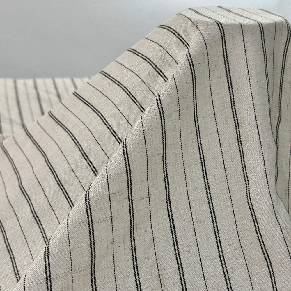 Ivory fabric with narrow black pinstripes is draped in broad, flowing folds, with more striped fabric visible behind it.