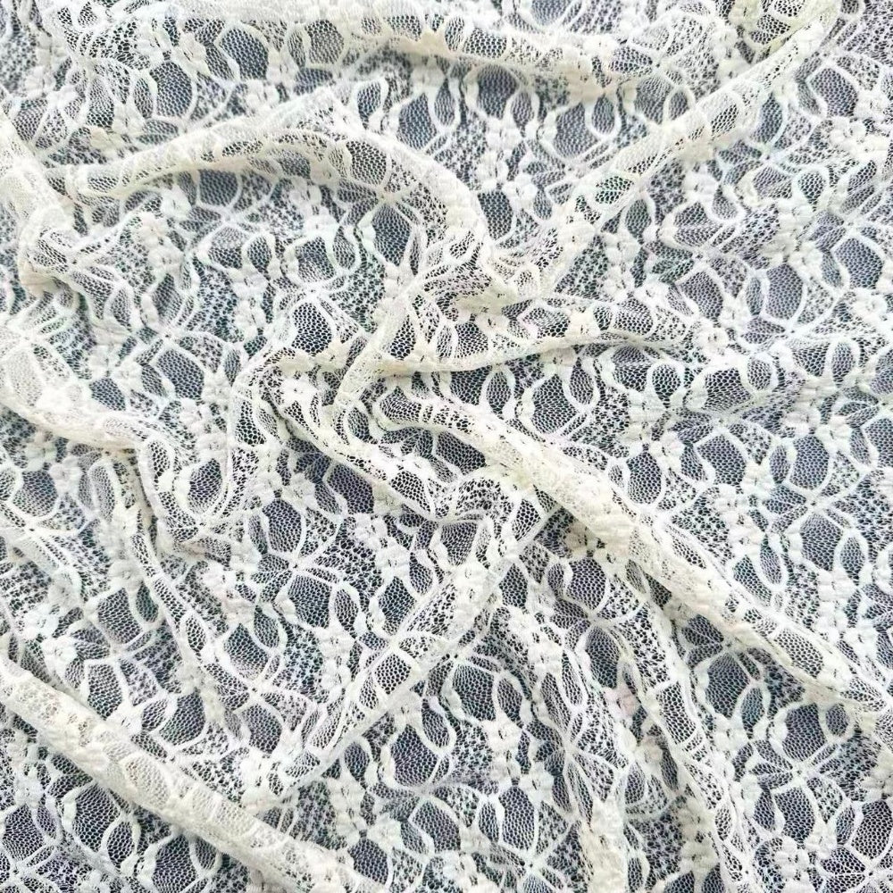 Close-up of ivory lace with an open mesh ground and dense floral motifs, arranged in overlapping draped folds.