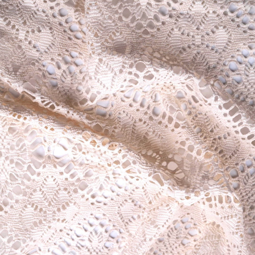 Close-up of pale ivory lace fabric arranged in loose folds, with an openwork pattern of small loops, scalloped bands, and raised oval details.