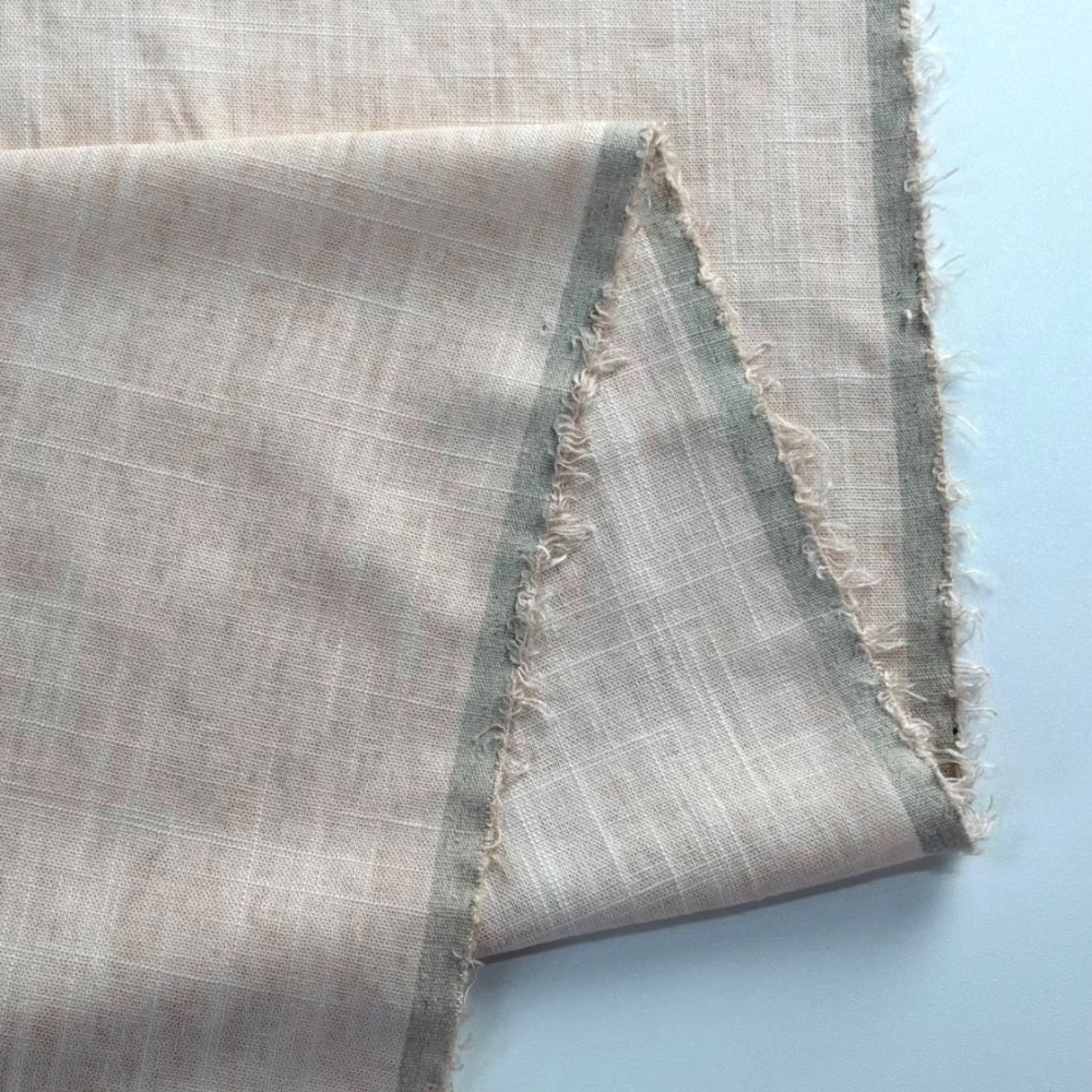 Pale gray-beige fabric with a fine white grid and muted gray-green stripes, arranged in overlapping folds with frayed edges against a light blue background.
