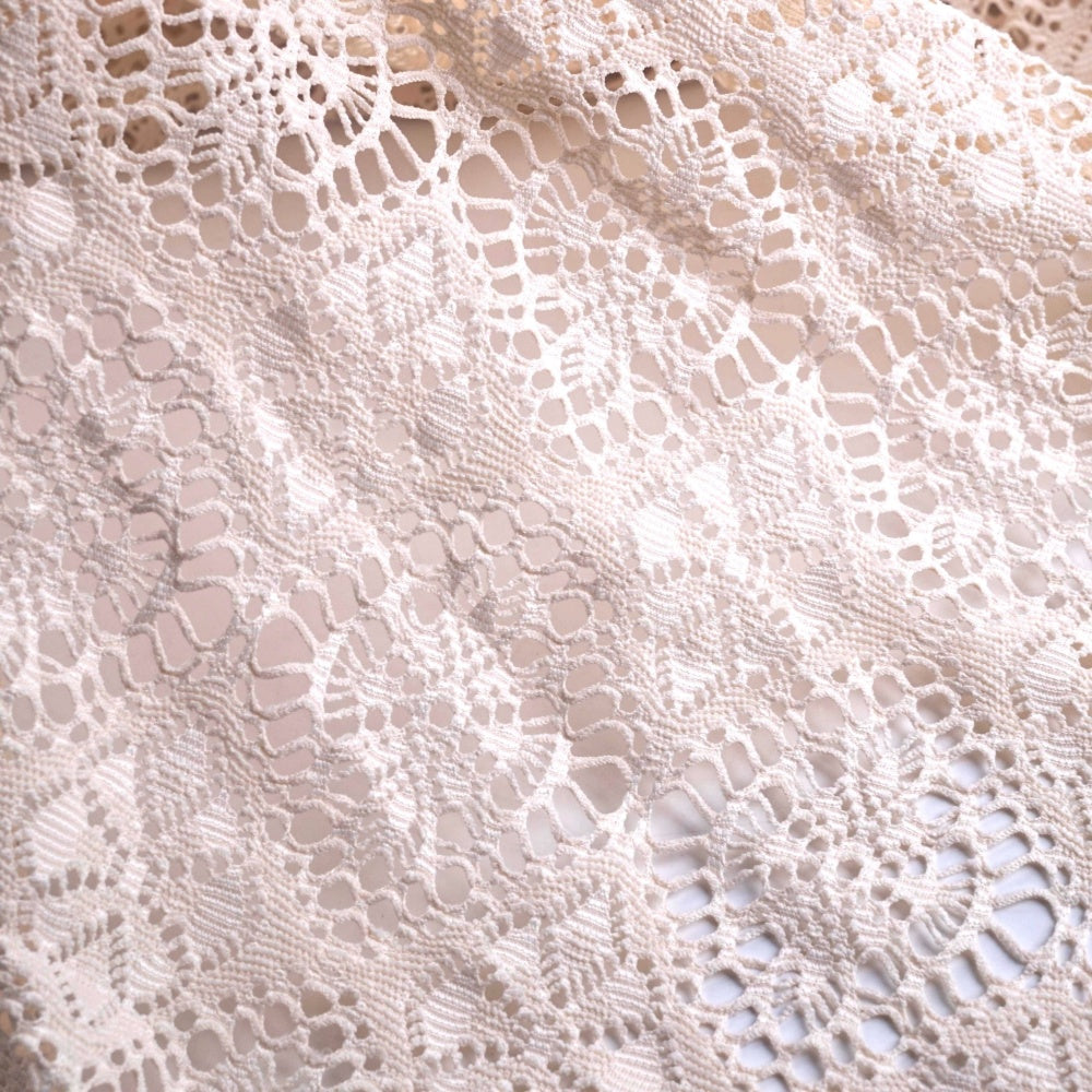 Close view of white lace fabric with an open, irregular floral and geometric pattern, spread flat across the frame.