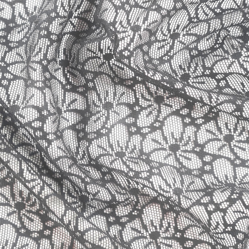 Close-up of layered black lace fabric with an irregular open grid and floral motifs over a light background.