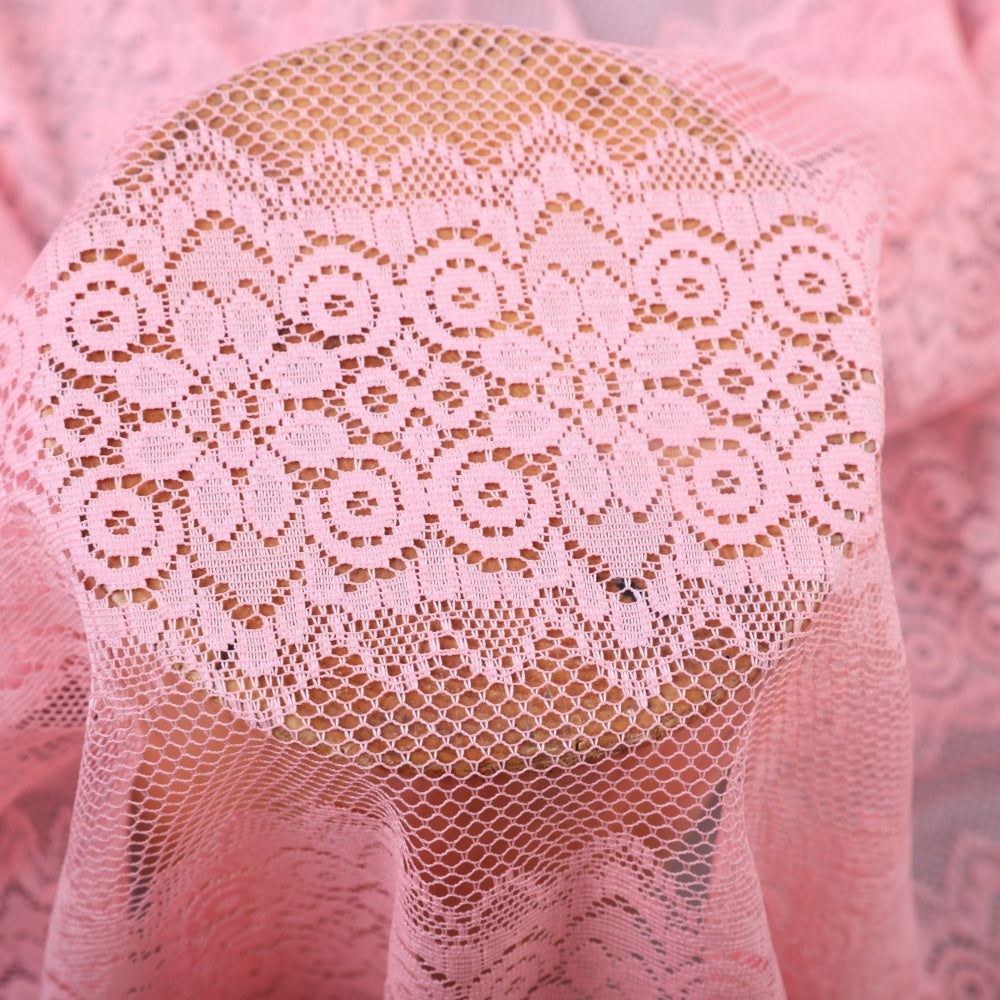 Close-up of pale pink lace cloth draped in curved folds, with rows of circular floral motifs, open mesh, and scalloped edges.