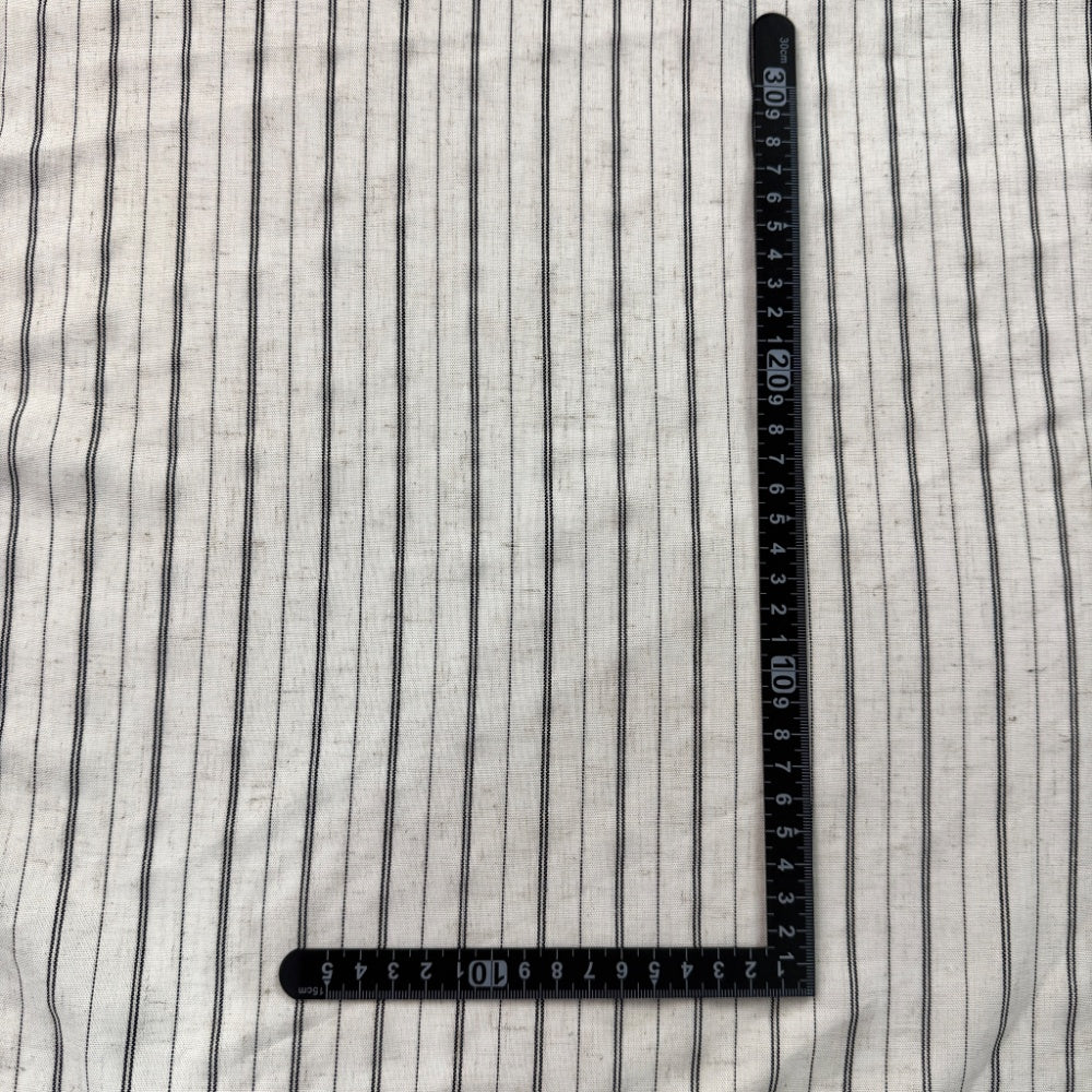 Off-white fabric with narrow, irregular black vertical stripes laid flat, with a black L-shaped measuring ruler placed on top.