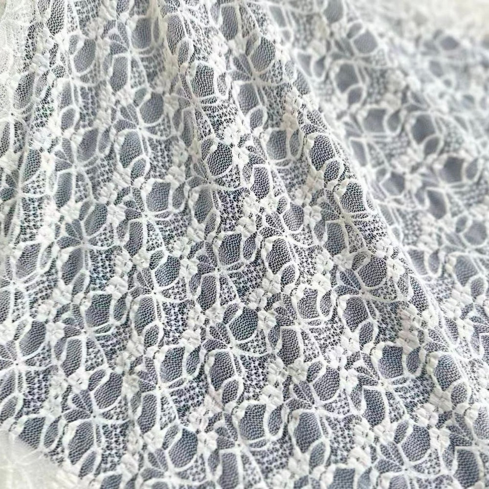 Close-up of white lace with a repeating floral motif and open mesh, draped in curved folds.