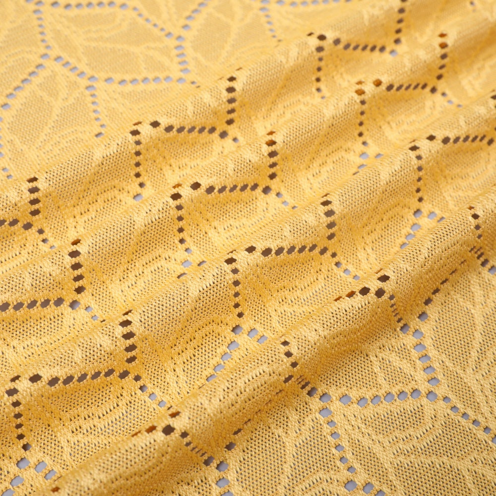 Close-up of golden yellow openwork fabric with repeating raised geometric bands and small diamond-shaped holes.