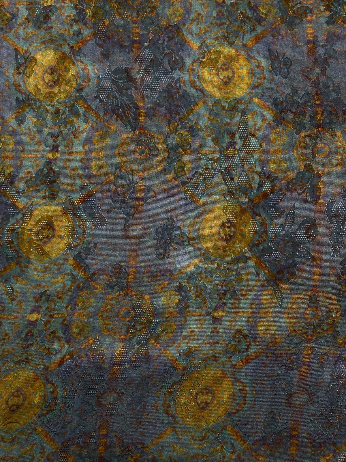 Close-up of a blue-gray fabric with repeating gold and rust circular motifs, arranged in a geometric pattern with scattered dotted details.