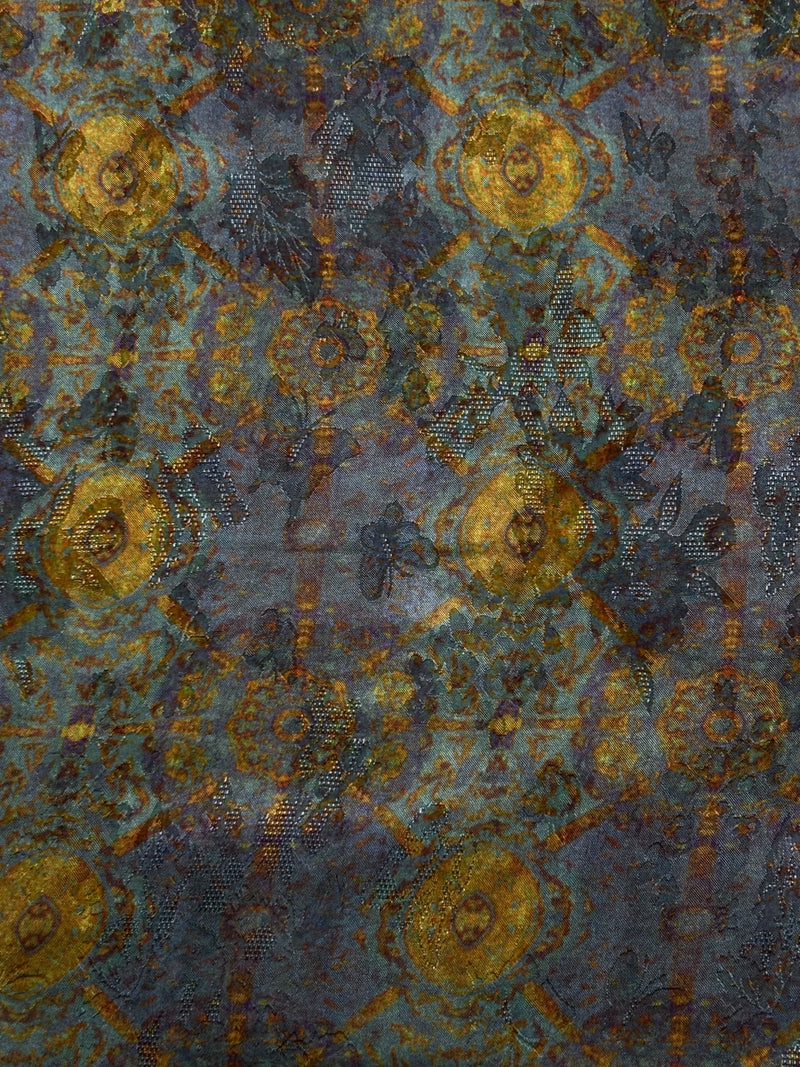 Close-up of a blue-gray fabric with repeating gold and rust circular motifs, arranged in a geometric pattern with scattered dotted details.