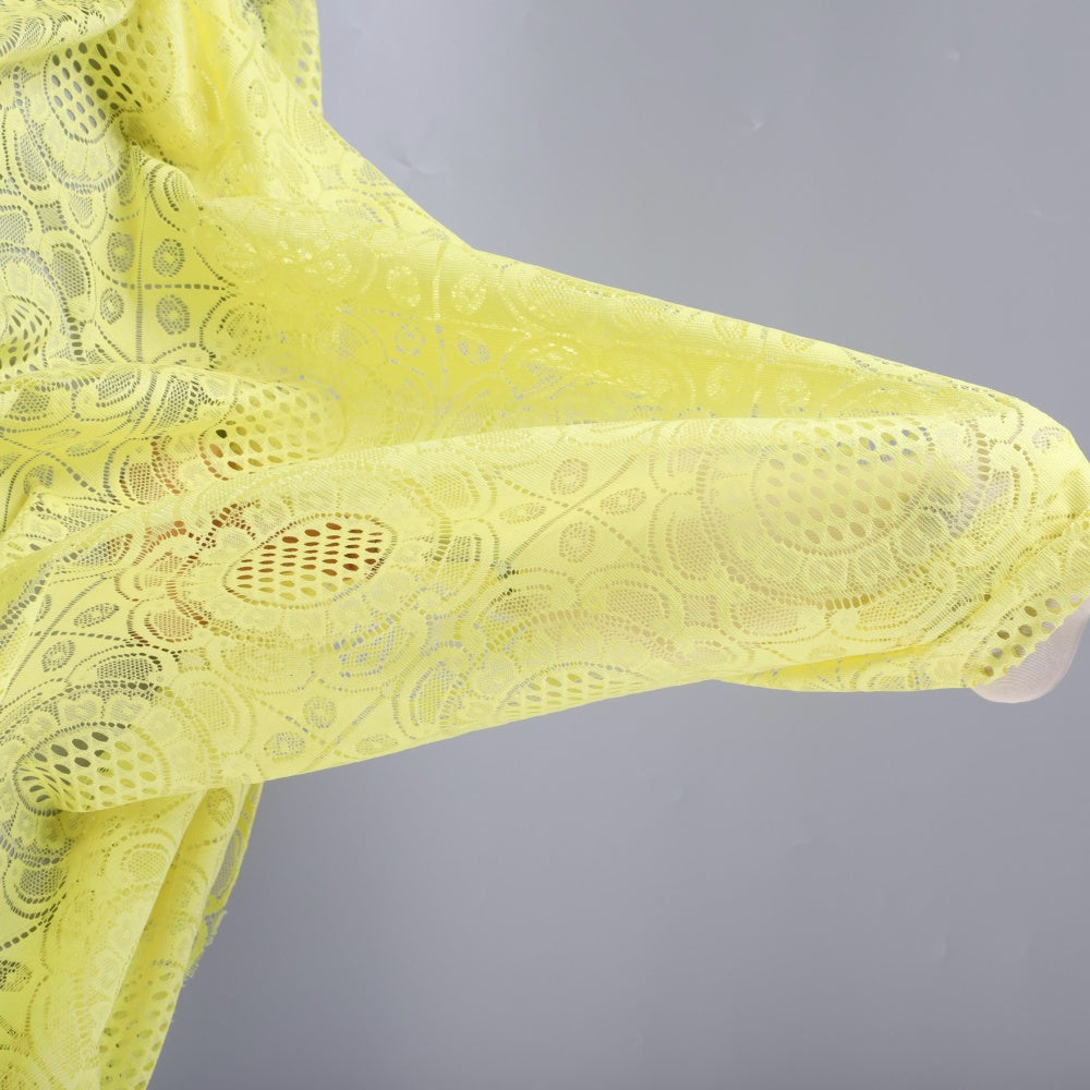 Pale yellow lace fabric with repeating floral and oval cutout motifs, draped in flowing folds against a gray background.