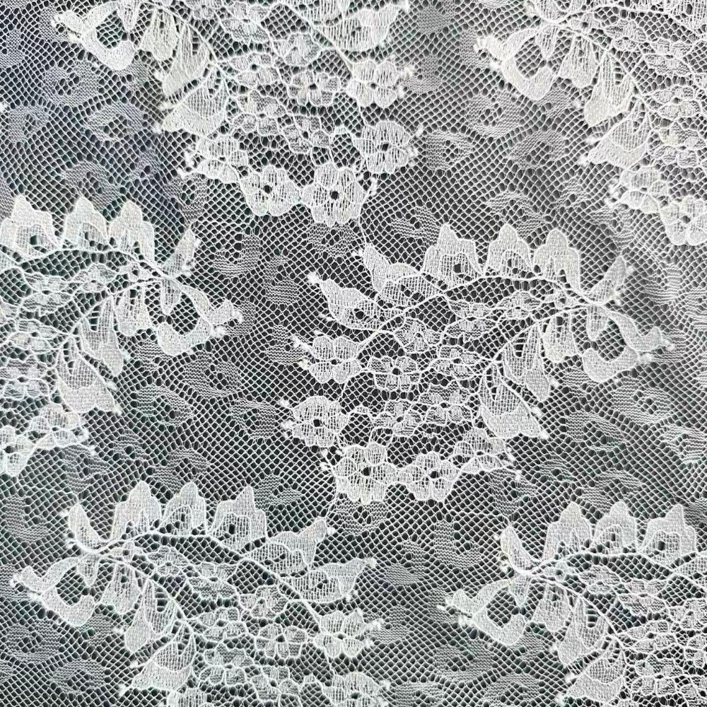 Close-up of white lace with a dense, repeating floral motif and fine mesh between the flowers.