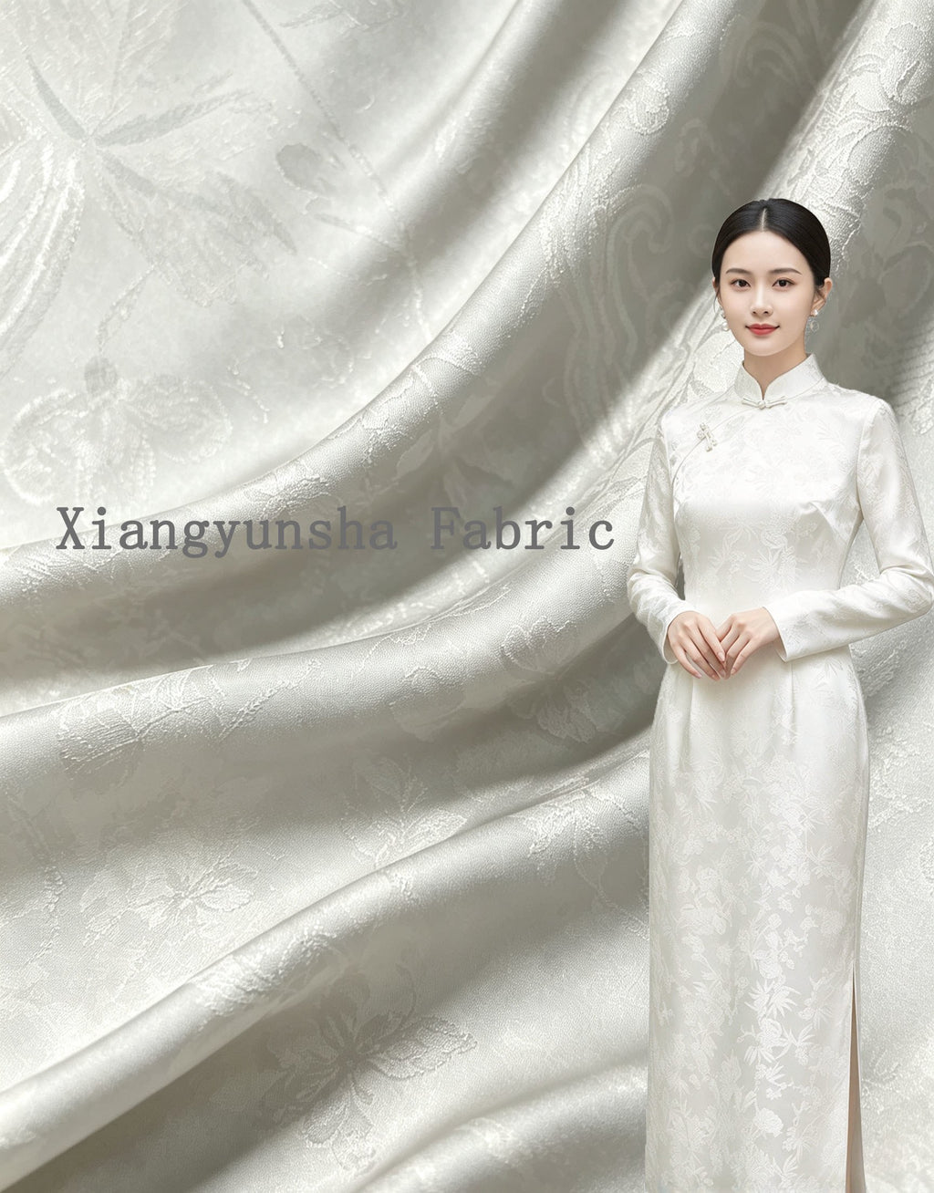 A woman wears a floor-length white garment with a subtle floral motif, posed against a backdrop of draped white and pale gray patterned fabric; full garment view.