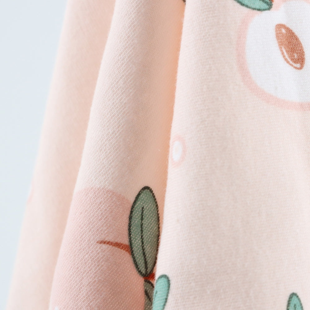 Close-up of pale peach cloth draped in curved folds, with a scattered print of muted green leaves and small rust-colored details.